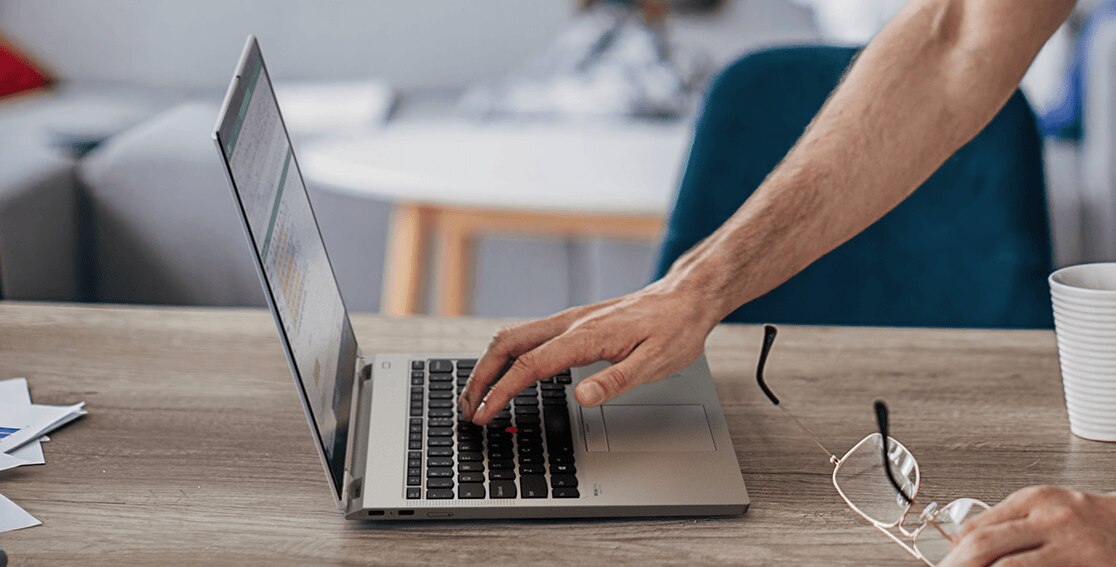 Left-side view of Lenovo ThinkPad Titanium Yoga laptop open on a counter, with a man’s right hand on keyboard. 
