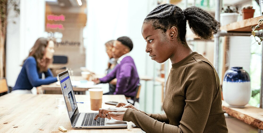 Woman in a café using the Lenovo ThinkPad Titanium Yoga laptop, left-side view. 