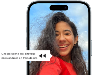 Un iPhone 15 montrant la fonctionnalité VoiceOver énonçant les informations figurant sur l'image : Une personne aux cheveux noirs ondulés en train de rire