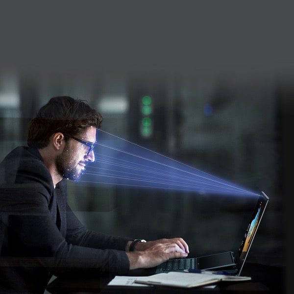 Un faisceau lumineux est projeté sur le visage d'un homme, indiquant que son visage est scanné par la caméra IR de l'ordinateur portable.