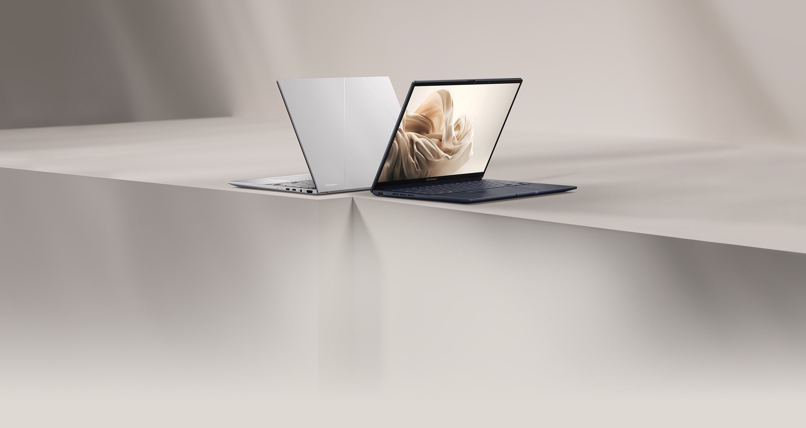 Un Zenbook 14 OLED Ponder Blue et Foggy Silver placé dans un open space blanc beige avec des lumières et des ombres.