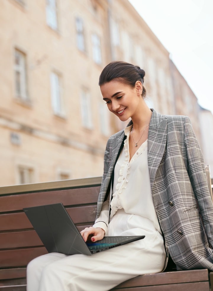 Une femme est assise sur un banc et utilise un ASUS Zenbook Duo.