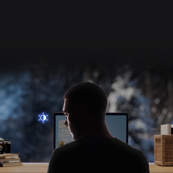 Un homme détourne le regard de l'écran de son ordinateur portable, qui semble faiblement éclairé.