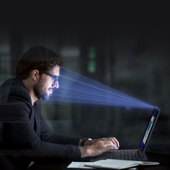 Un faisceau lumineux est projeté sur le visage d'un homme, indiquant que son visage est scanné par la caméra IR de l'ordinateur portable.